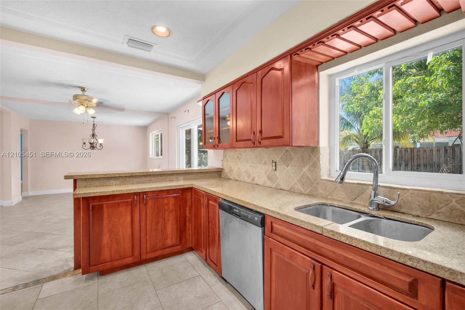 Kitchen featuring cherry-finish cabinetry, stone-texture countertops, a dual-basin stainless steel sink with gooseneck faucet, diagonal-set ceramic tile backsplash, and tile flooring