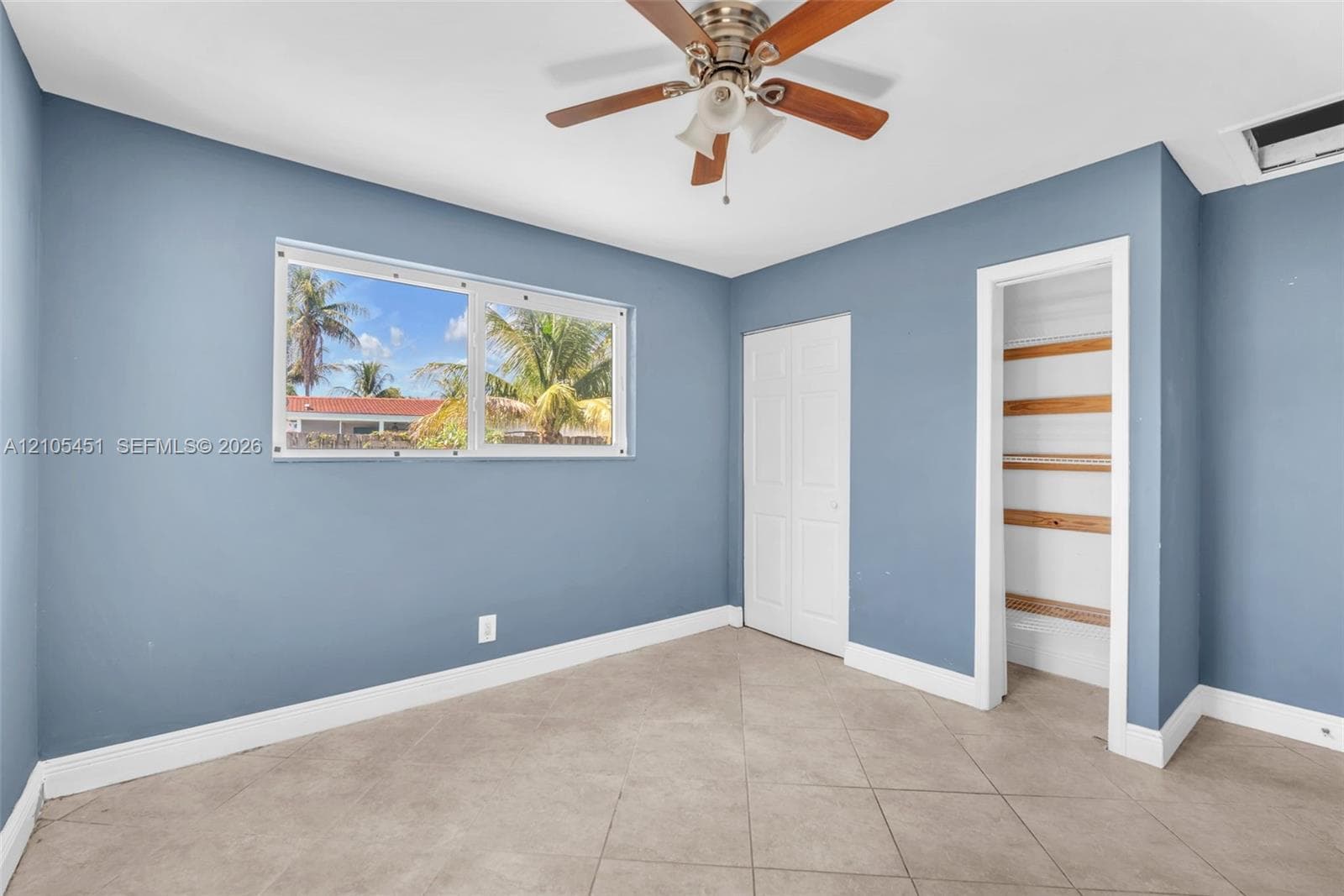 Bedroom featuring tile flooring, ceiling fan with integrated lighting, dual-pane window, and a closet with built-in shelving