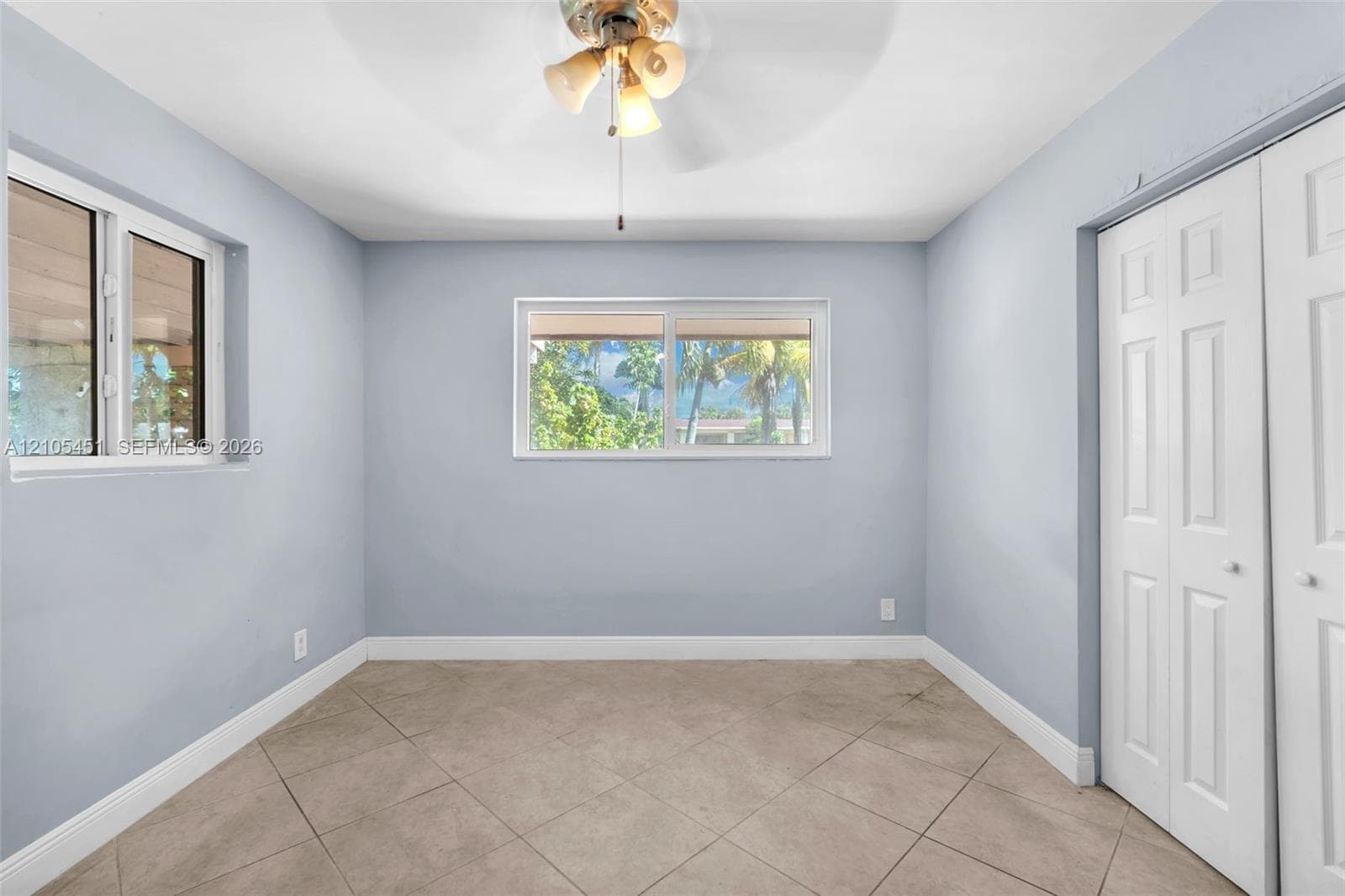 Neutral-toned room featuring large-format tile flooring, sliding windows with exterior palm tree scenery, and a built-in closet with paneled double doors