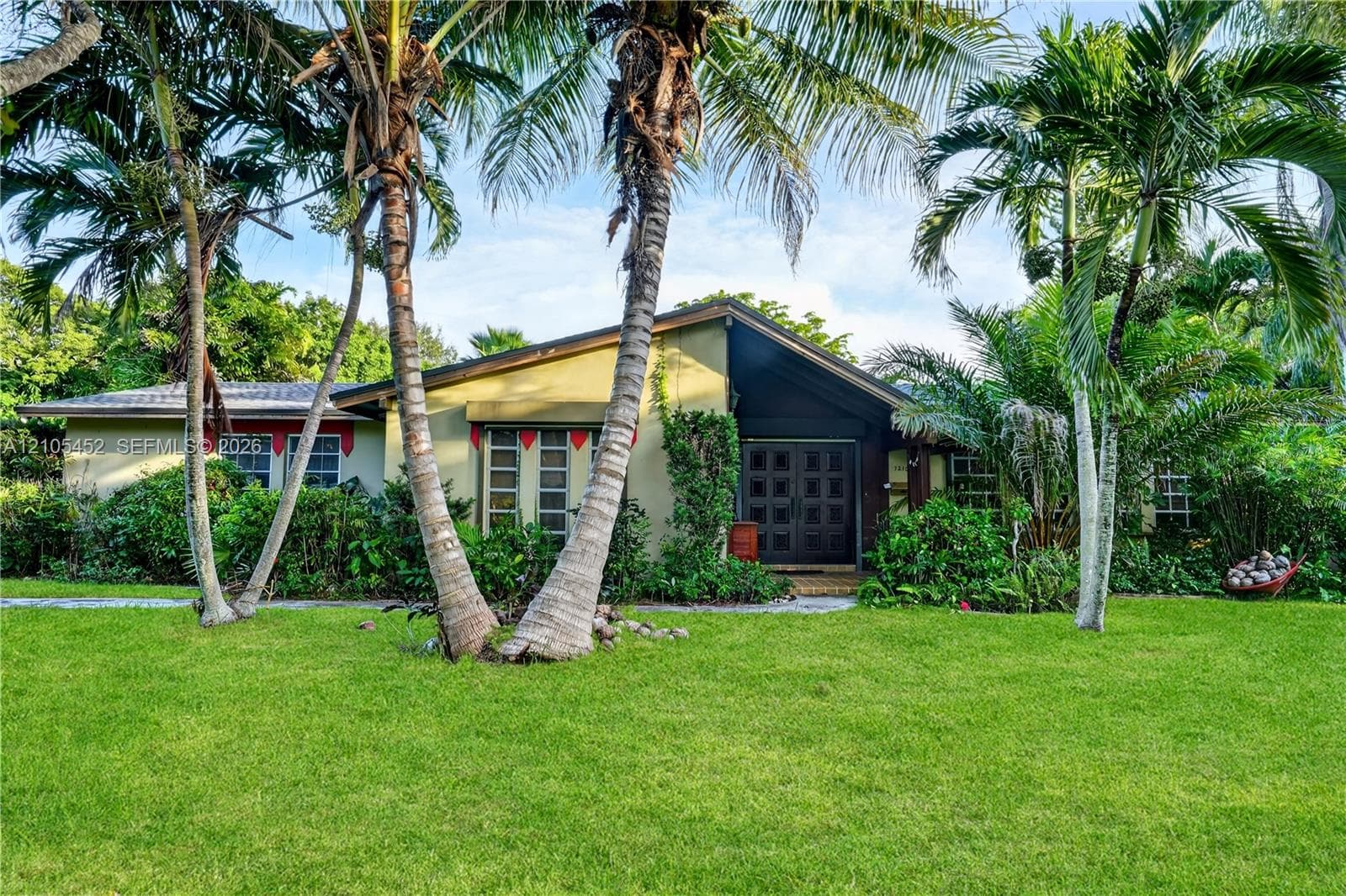 Single-story exterior featuring a low-pitch roofline, double front entry doors, multi-pane windows, and mature palm trees