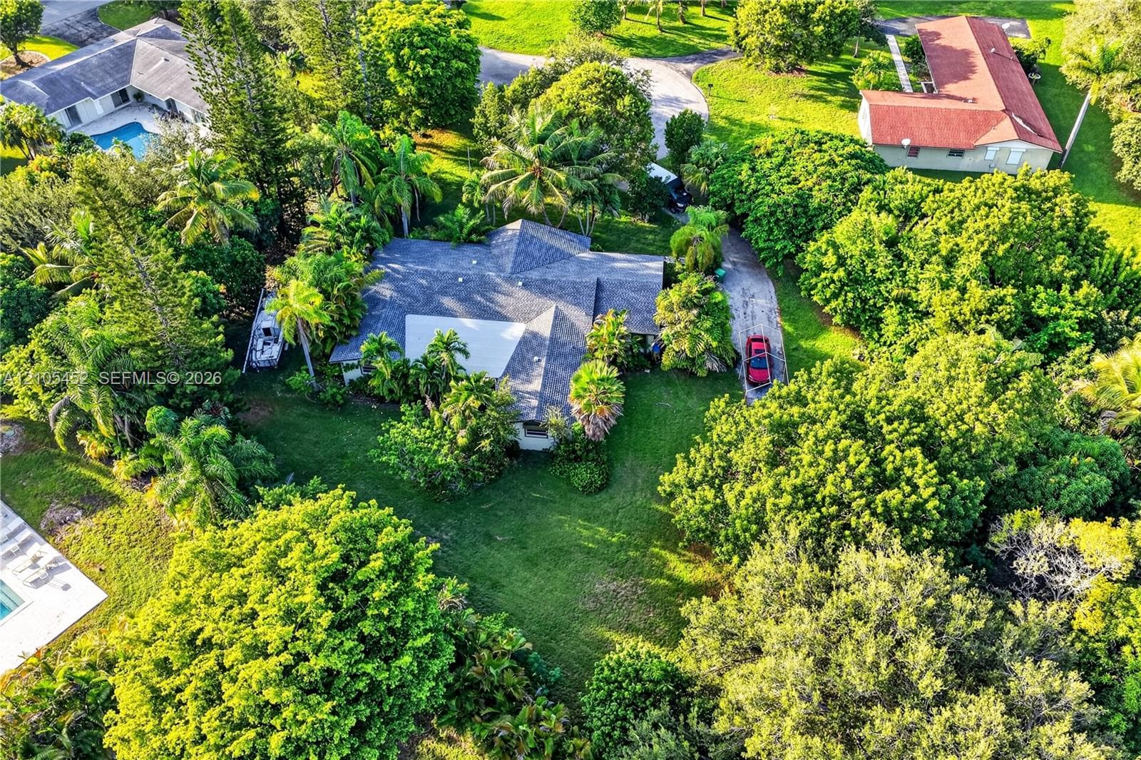 Aerial perspective featuring a shingled roofline, concrete driveway, and expansive grounds with mature trees and dense perimeter vegetation