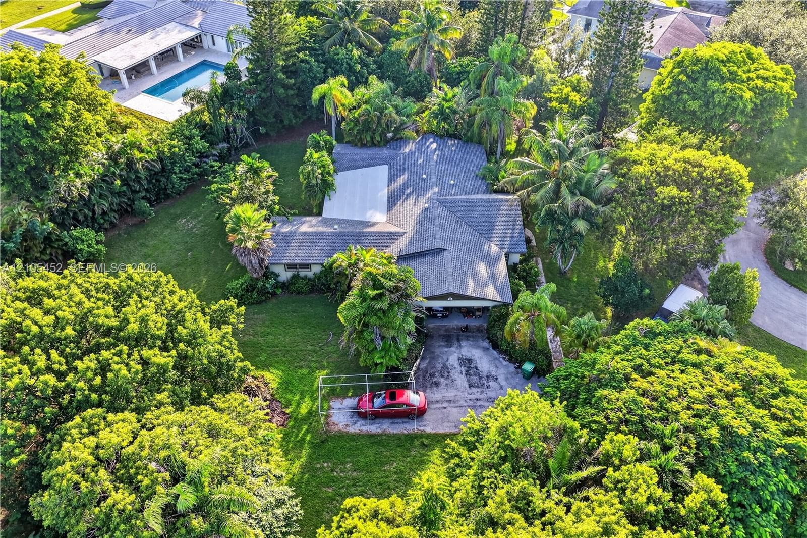 Aerial perspective of a multi-gabled residence featuring a multi-car driveway, substantial tree canopy, and established landscaping