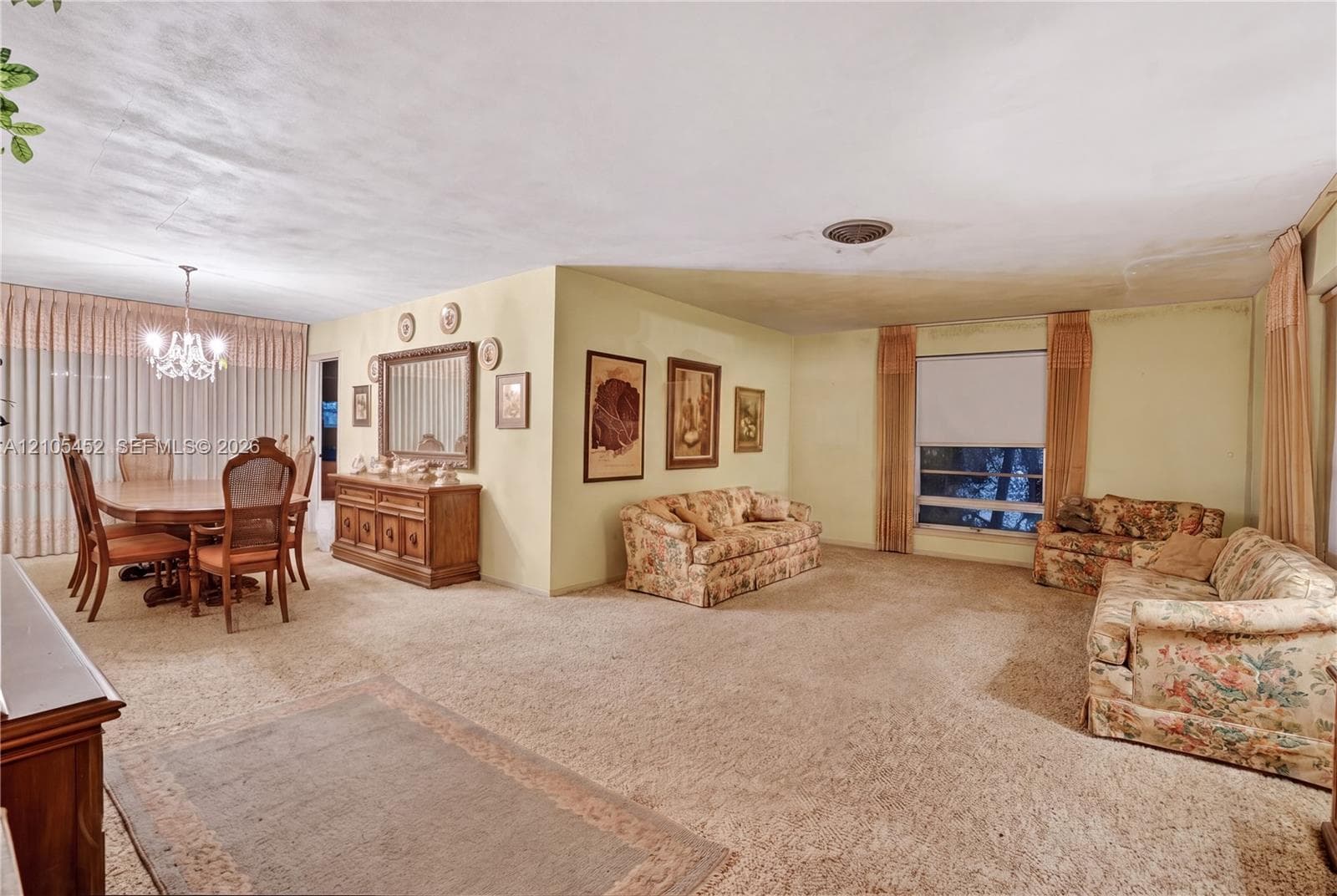 Open-concept living and dining area featuring a central built-in wood credenza, decorative ceiling-mounted chandelier, and expansive windows