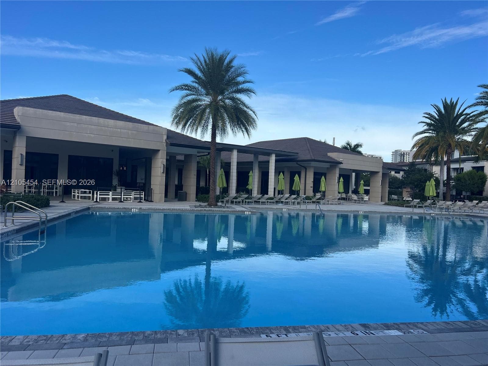 Expansive outdoor pool with integrated steps, surrounded by a paved deck and a covered patio area with recessed lighting