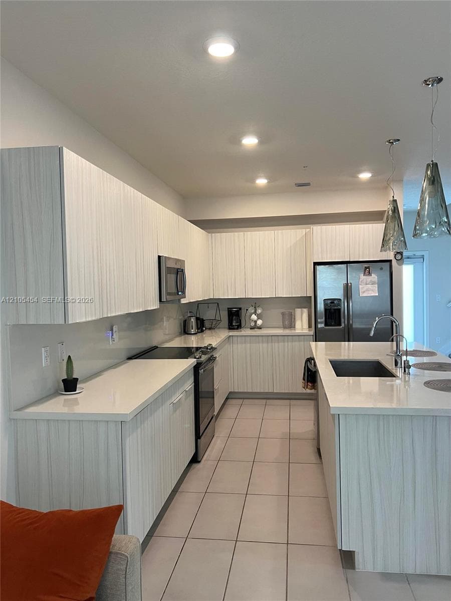 Contemporary kitchen featuring white cabinetry, light-toned countertops, stainless steel appliances, and an island with an integrated sink