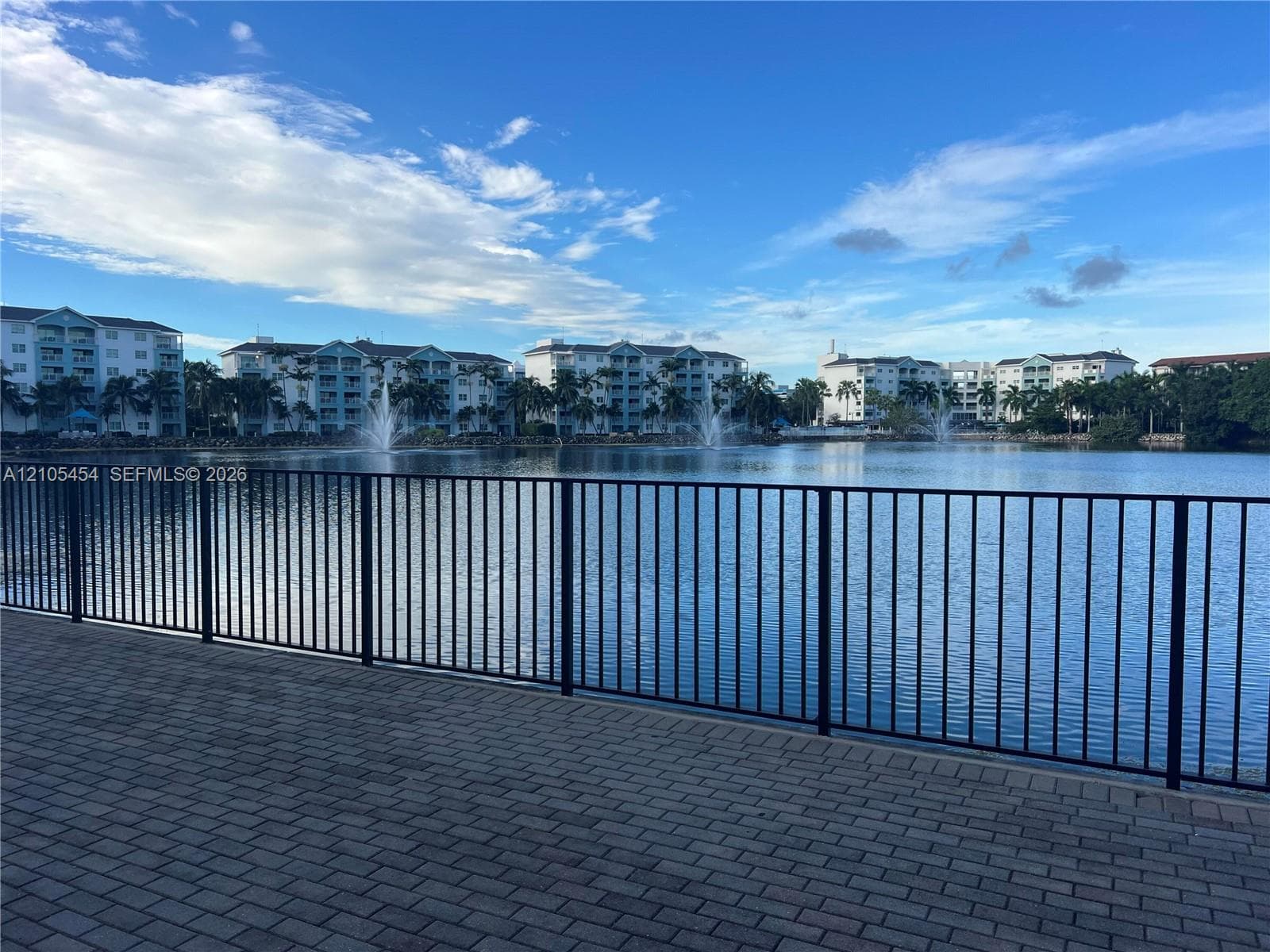 Paver patio with black metal railing overlooking a tranquil lake with water features