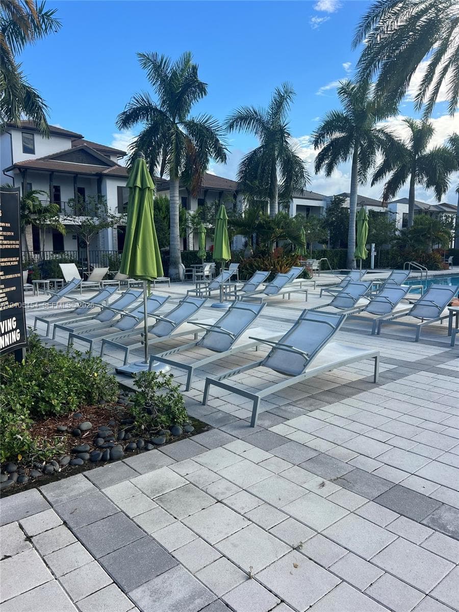 Expansive pool deck featuring paver flooring, multiple lounge chairs, and mature palm trees