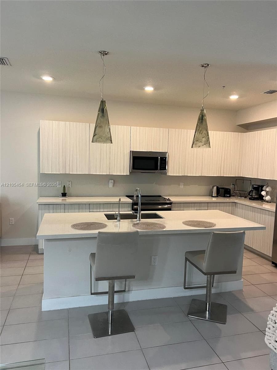 Modern kitchen featuring white cabinetry, a large kitchen island with integrated sink, recessed lighting, and two pendant light fixtures
