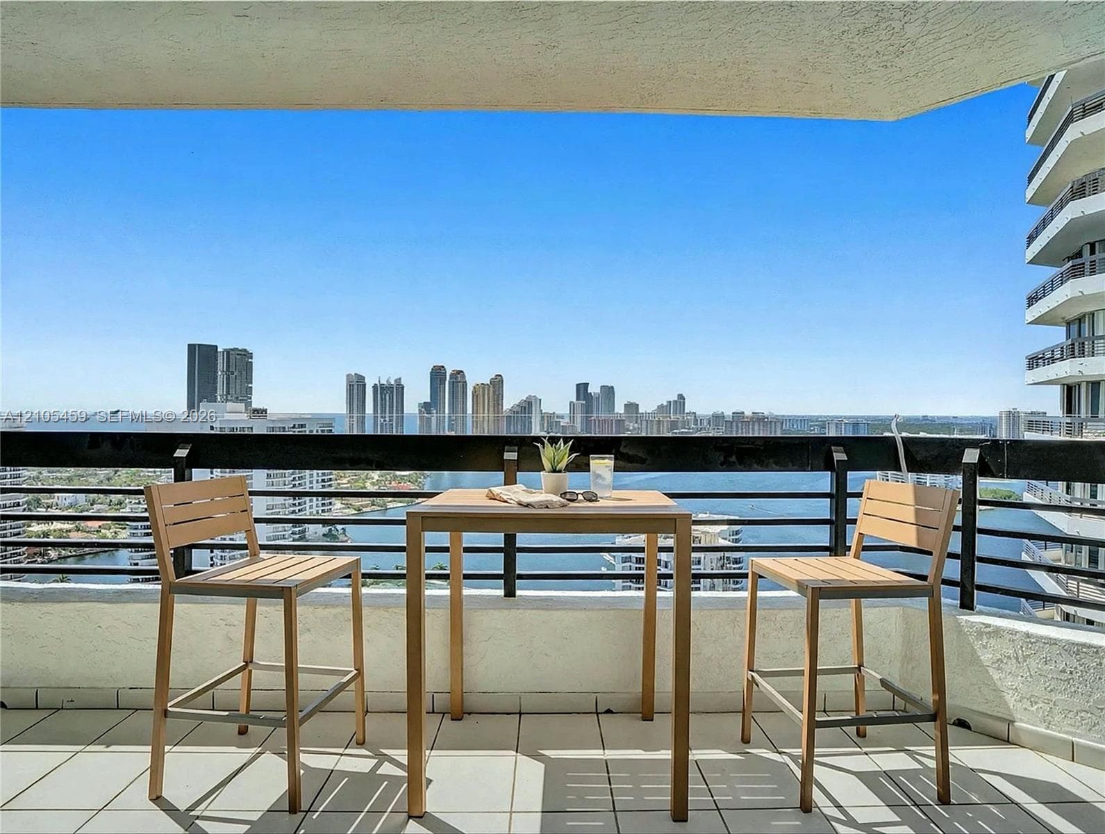 Expansive balcony with tiled flooring, black metal railing, and high-rise city scenery