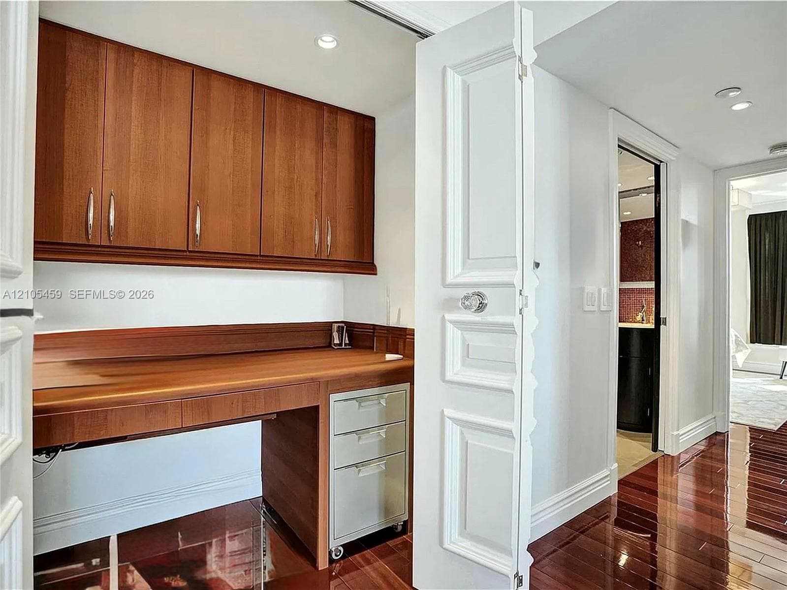 Built-in wood-finish desk with coordinating upper cabinetry, wood-finish flooring, recessed lighting, and panel-style doors