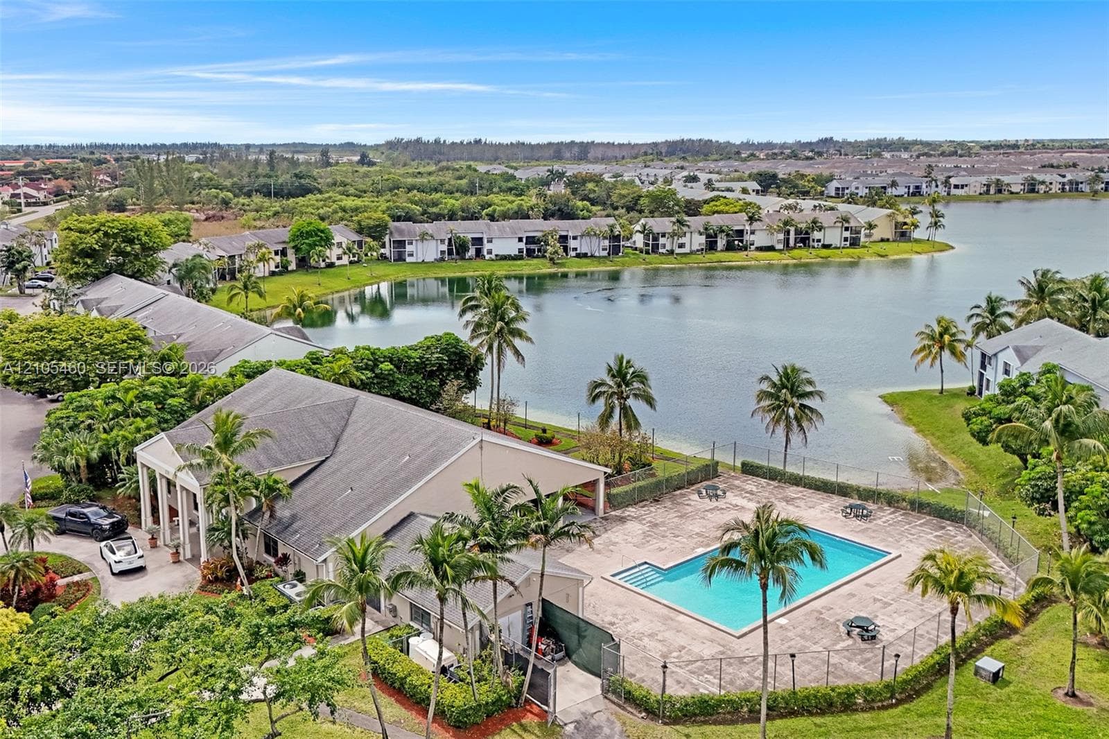 Community pool with a surrounding fence, large body of water, and extensive green landscaping