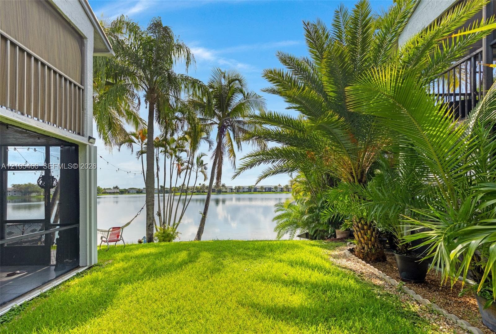 Lakeside property featuring mature palm trees, a well-maintained lawn, screened patio, and a second-story balcony
