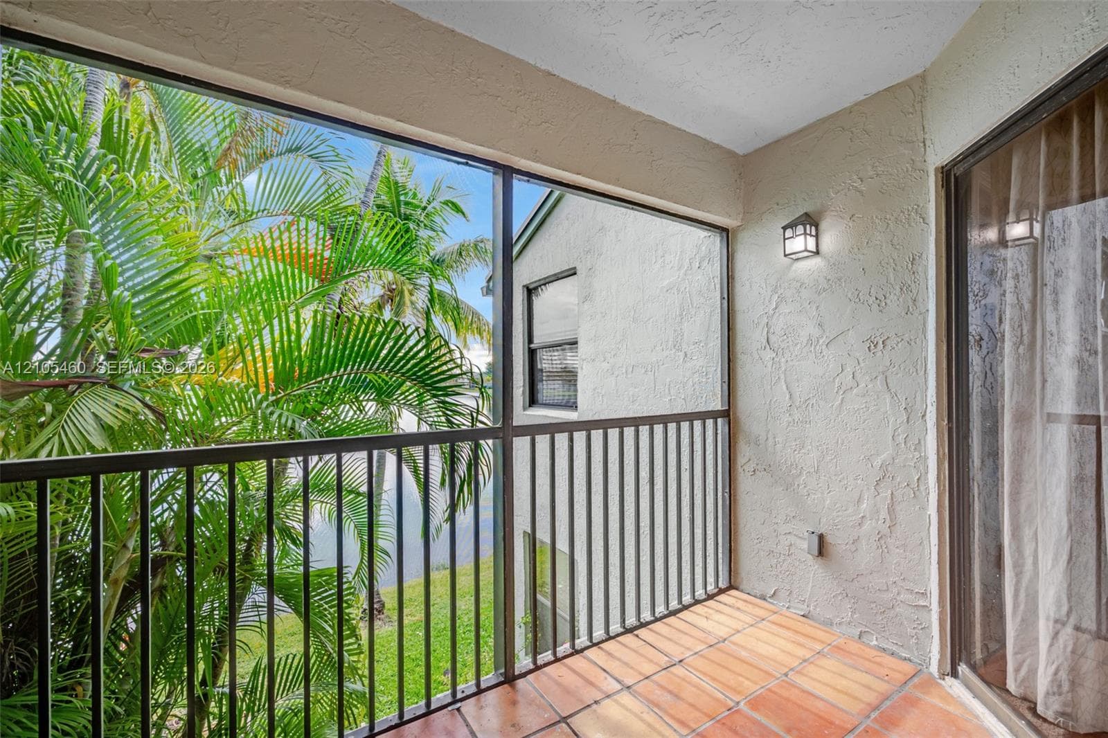 Screened balcony featuring terracotta tile flooring, metal railings, and an outdoor wall sconce