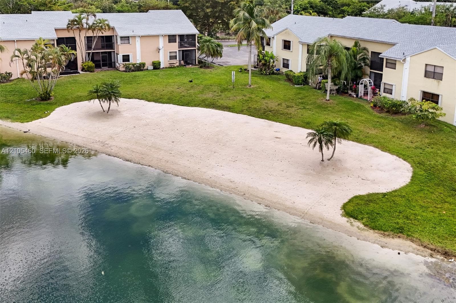 Expansive waterfront property featuring a private sandy beach, mature palm trees, and lush green landscaping