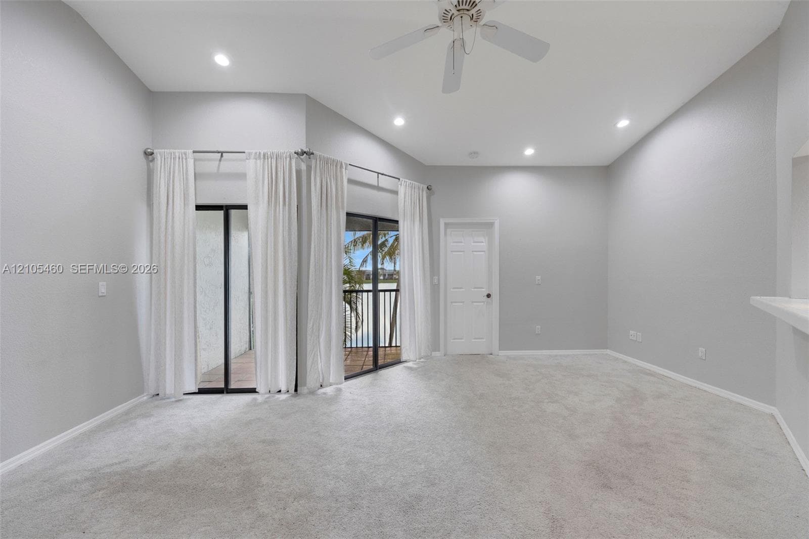 Vaulted ceilings with recessed lighting, ceiling fan, carpeted flooring, and a glass sliding door leading to an outdoor balcony