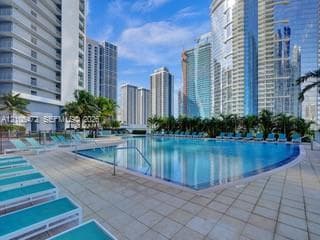 Expansive pool deck with a curved swimming pool, surrounded by paver tile flooring, and mature palm trees