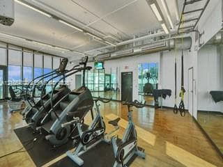 Expansive fitness area featuring floor-to-ceiling windows, wood-finish flooring, a full-length mirrored wall, and exposed ductwork