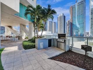Outdoor entertaining area featuring a built-in grill station, tile patio, and established landscaping