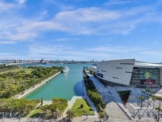Waterfront setting featuring a modern structure, green spaces, and a prominent bridge