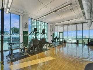 Expansive room with wood-finish flooring, floor-to-ceiling windows, roller shades, exposed overhead ductwork, and track lighting