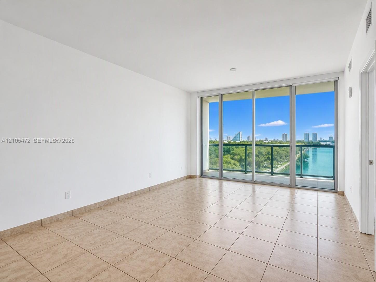 Neutral-toned tile flooring, floor-to-ceiling sliding glass doors, and a glass-paneled balcony featuring water and cityscape scenery