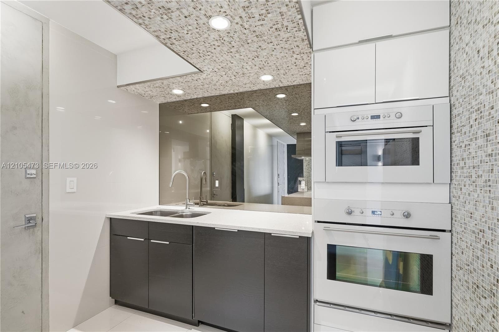 Integrated wall oven and microwave with sleek white cabinetry, mosaic tile accent wall, and recessed lighting
