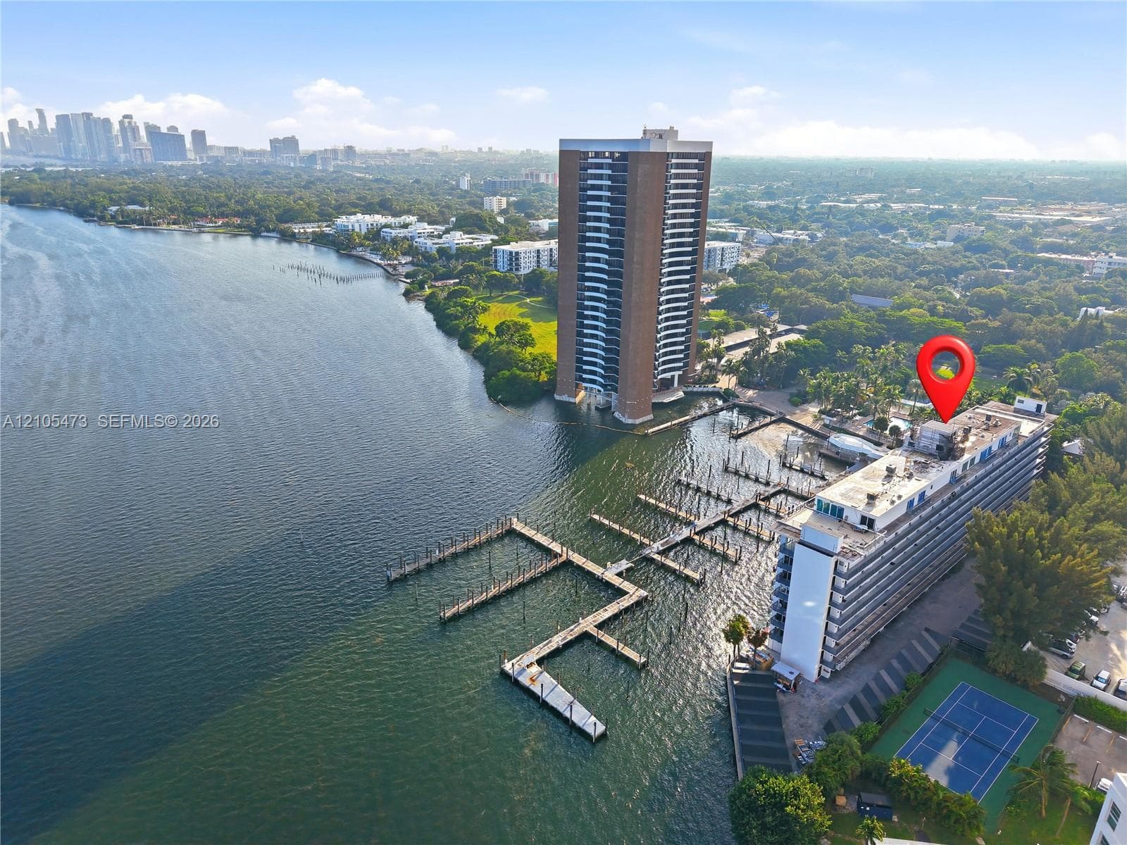 Waterfront property featuring extensive boat slips, a tennis court, and a high-rise building with multiple balconies