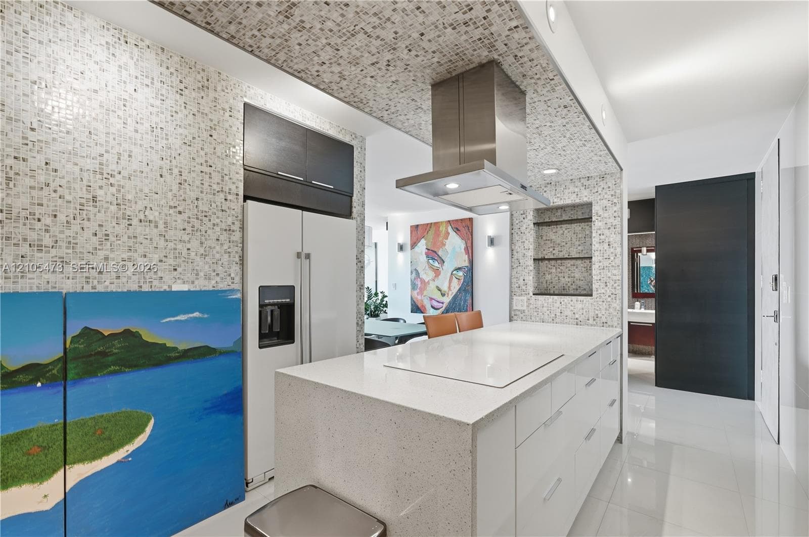 Gourmet kitchen with a large central island, white cabinetry, stainless steel range hood, and mosaic tile backsplash and ceiling accent