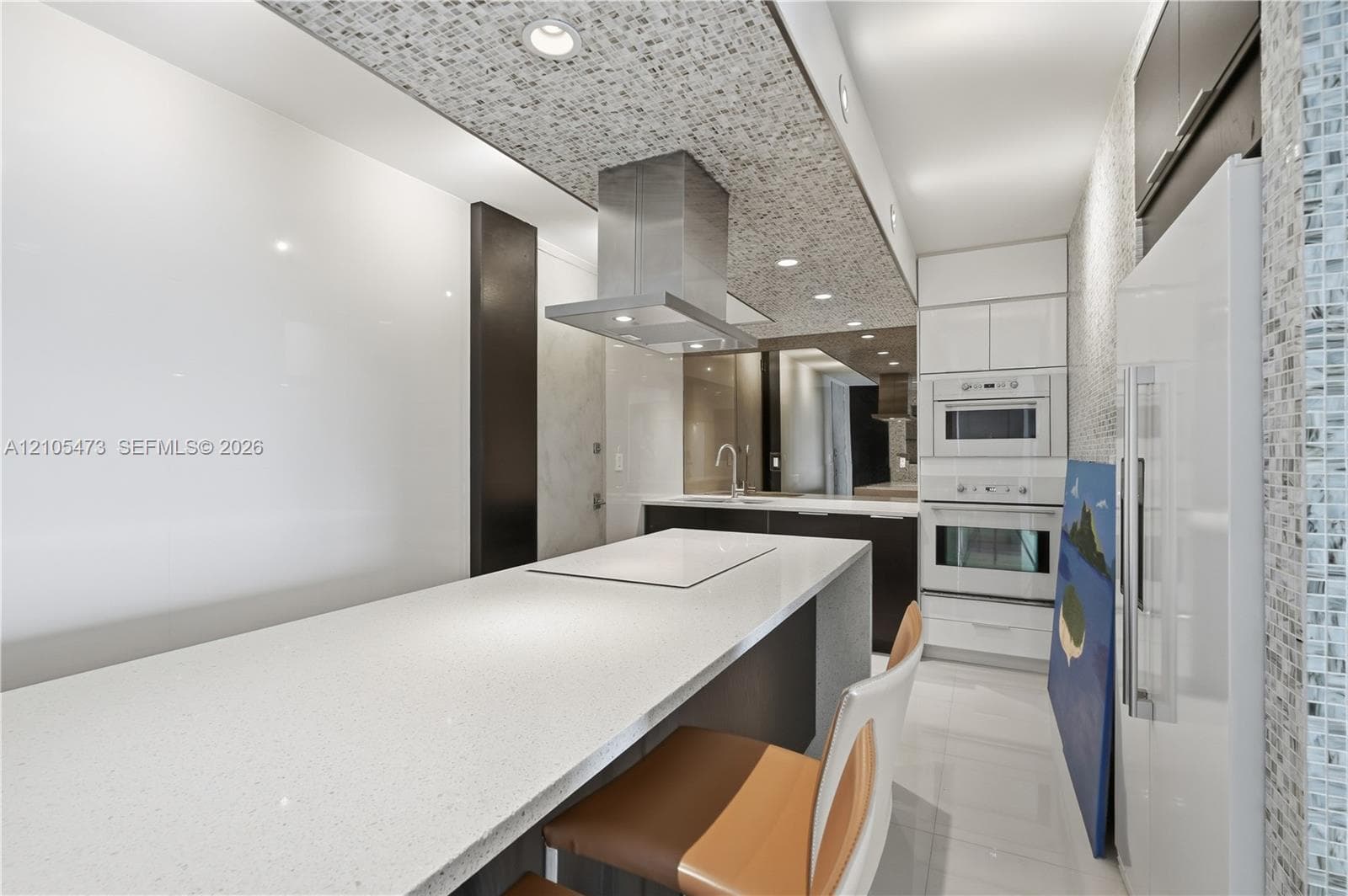 Kitchen featuring a built-in cooktop, stainless steel range hood, integrated wall oven and microwave, and white built-in refrigerator