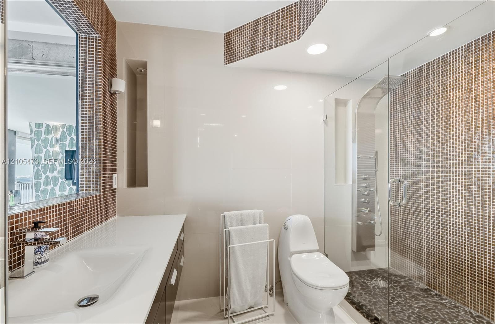 Glass-enclosed shower with pebble-finish flooring and mosaic tile surround