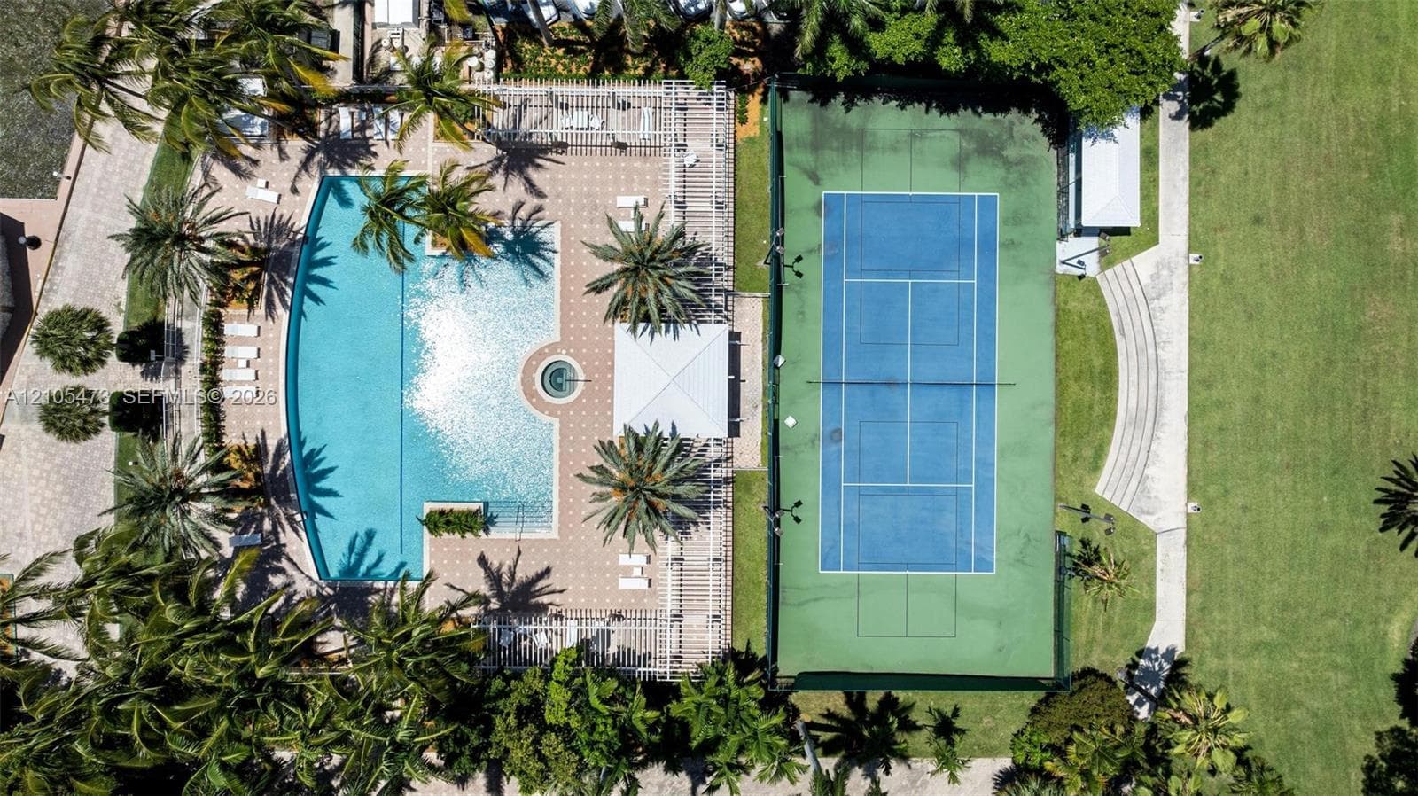Recreational area featuring a curvilinear swimming pool with an integrated spa, a paved deck, a hard-court tennis surface, and expansive lawn space