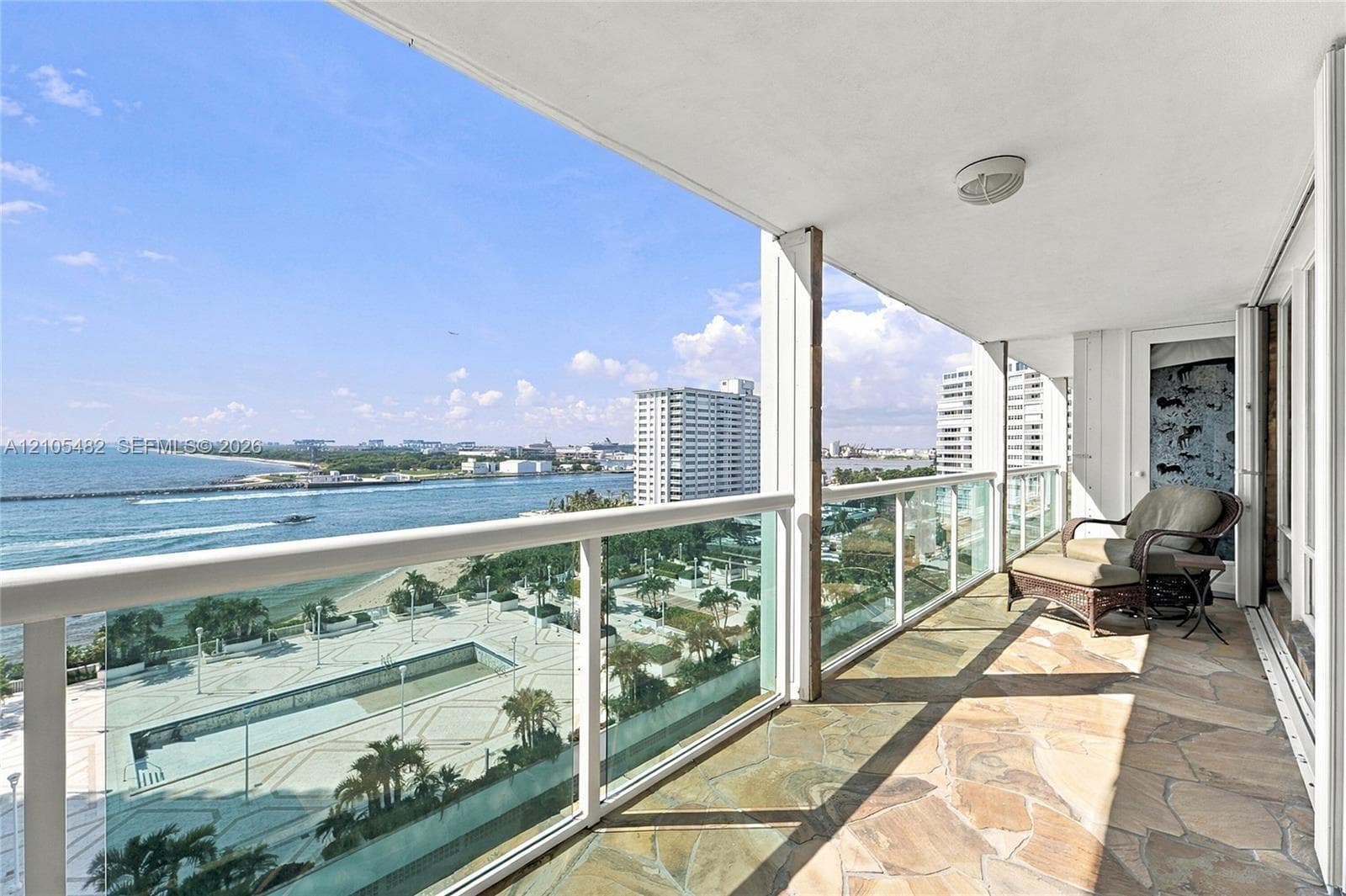 Covered balcony featuring flagstone flooring, glass panel railings, and expansive ocean and coastal vistas