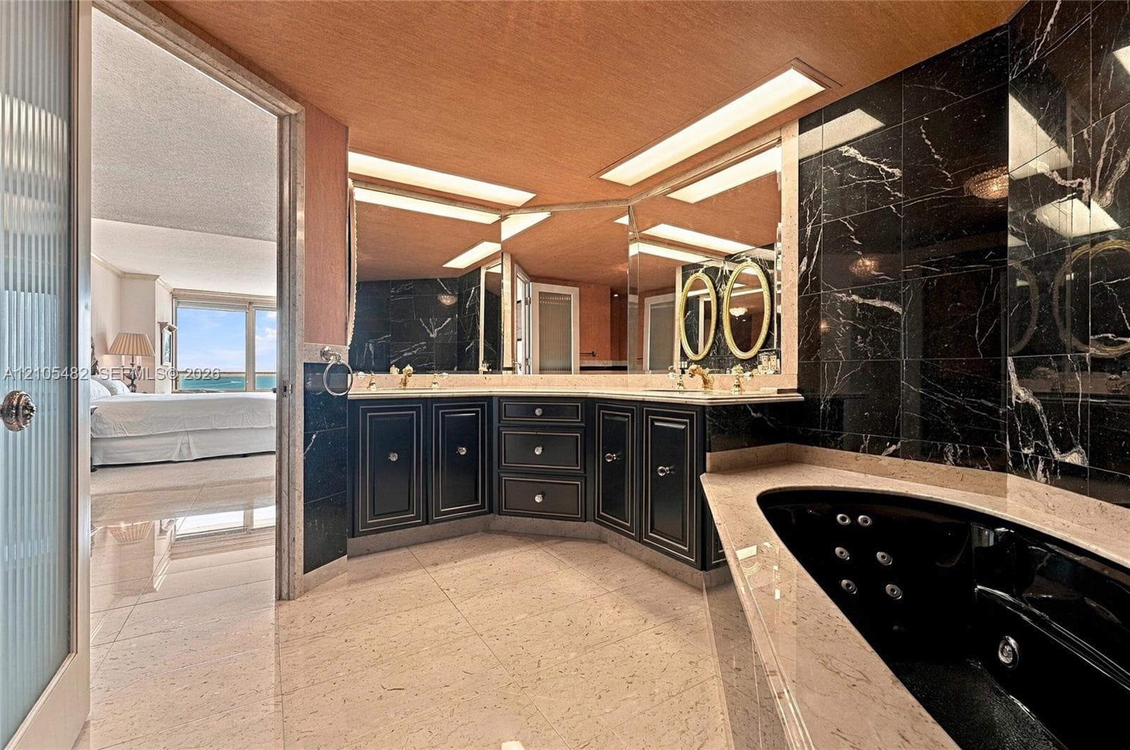 Bathroom featuring a black soaking tub with jetted nozzles, stone-finish surround, dark cabinetry, recessed lighting, and a floor-to-ceiling mirror