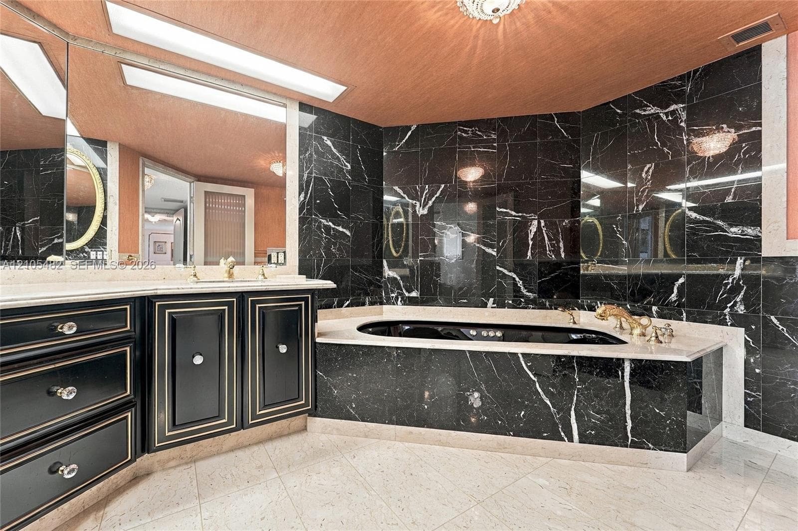 Jetted soaking tub with stone surround, custom black cabinetry with metallic trim, light-toned stone flooring, full-wall mirrors, and recessed lighting