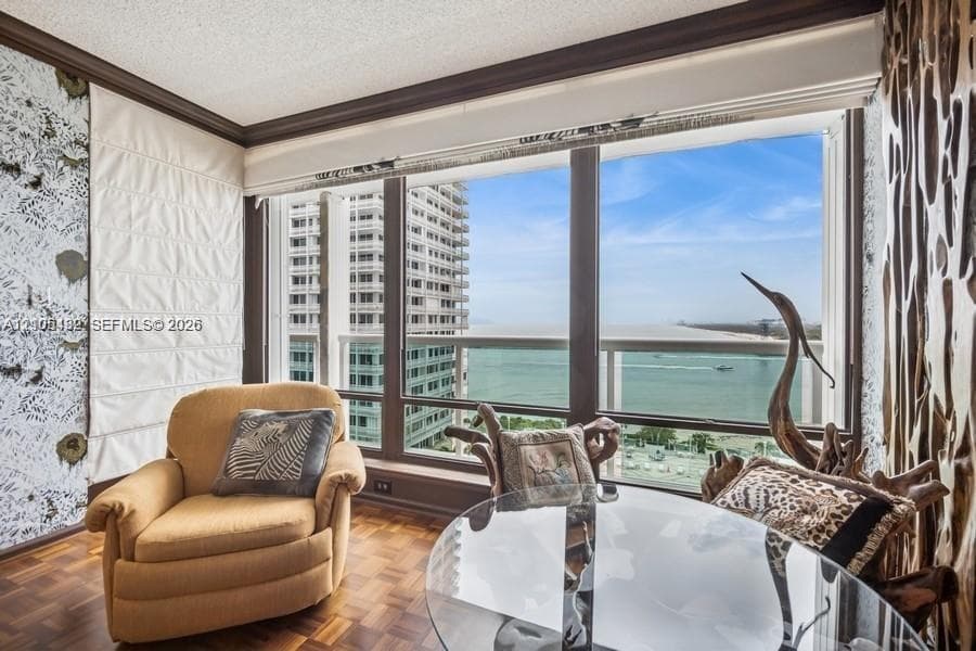 Large floor-to-ceiling windows, parquet wood flooring, crown molding, and a private balcony featuring a water backdrop