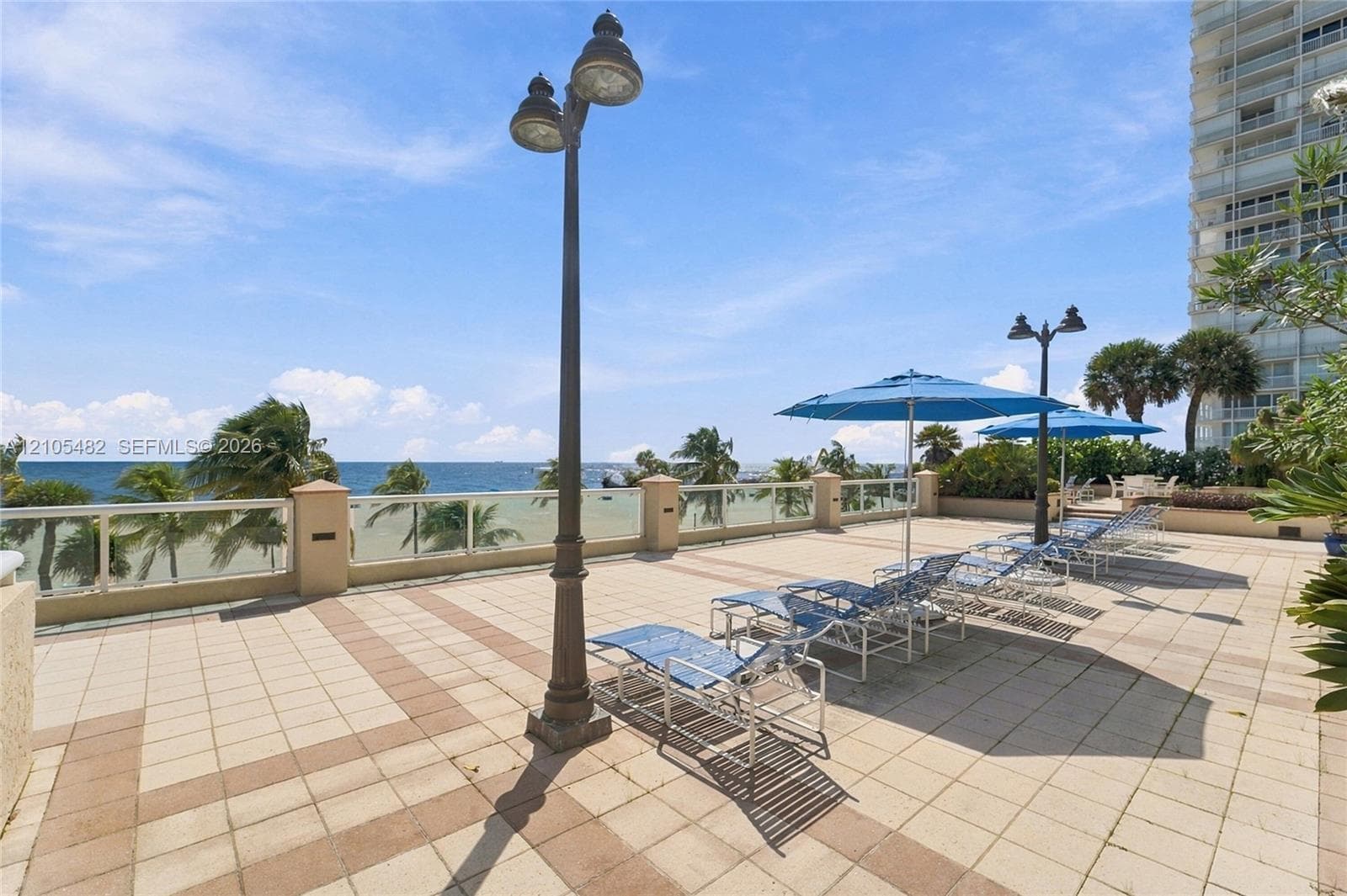 Expansive terrace featuring decorative paver flooring, perimeter glass railing, and tall metal lamp posts