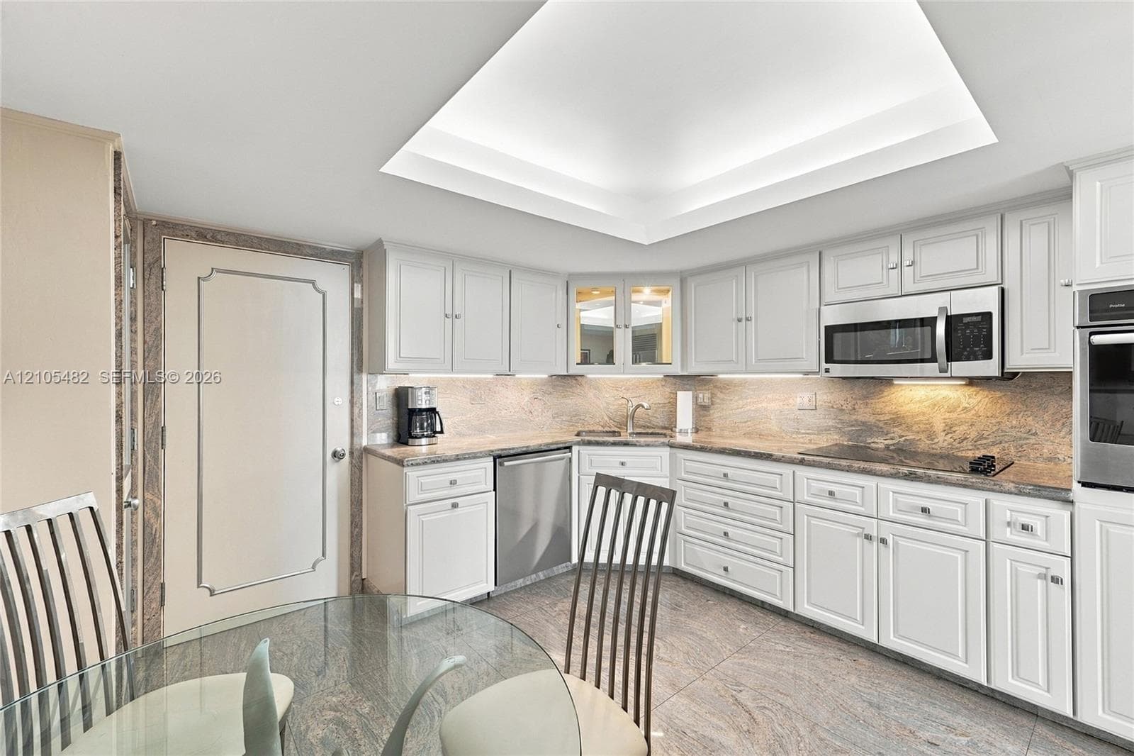 Kitchen featuring white shaker-style cabinetry, stone countertops, stainless steel appliances, recessed tray ceiling, and stone flooring