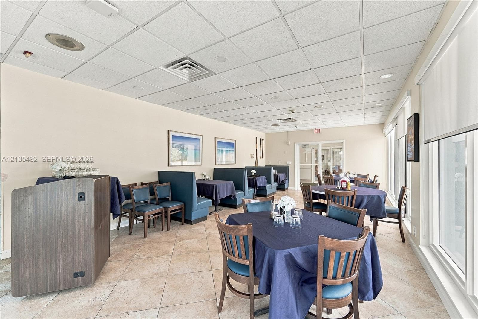 Spacious interior room featuring tile flooring, a drop ceiling with recessed lighting, and a large window wall with retractable shades