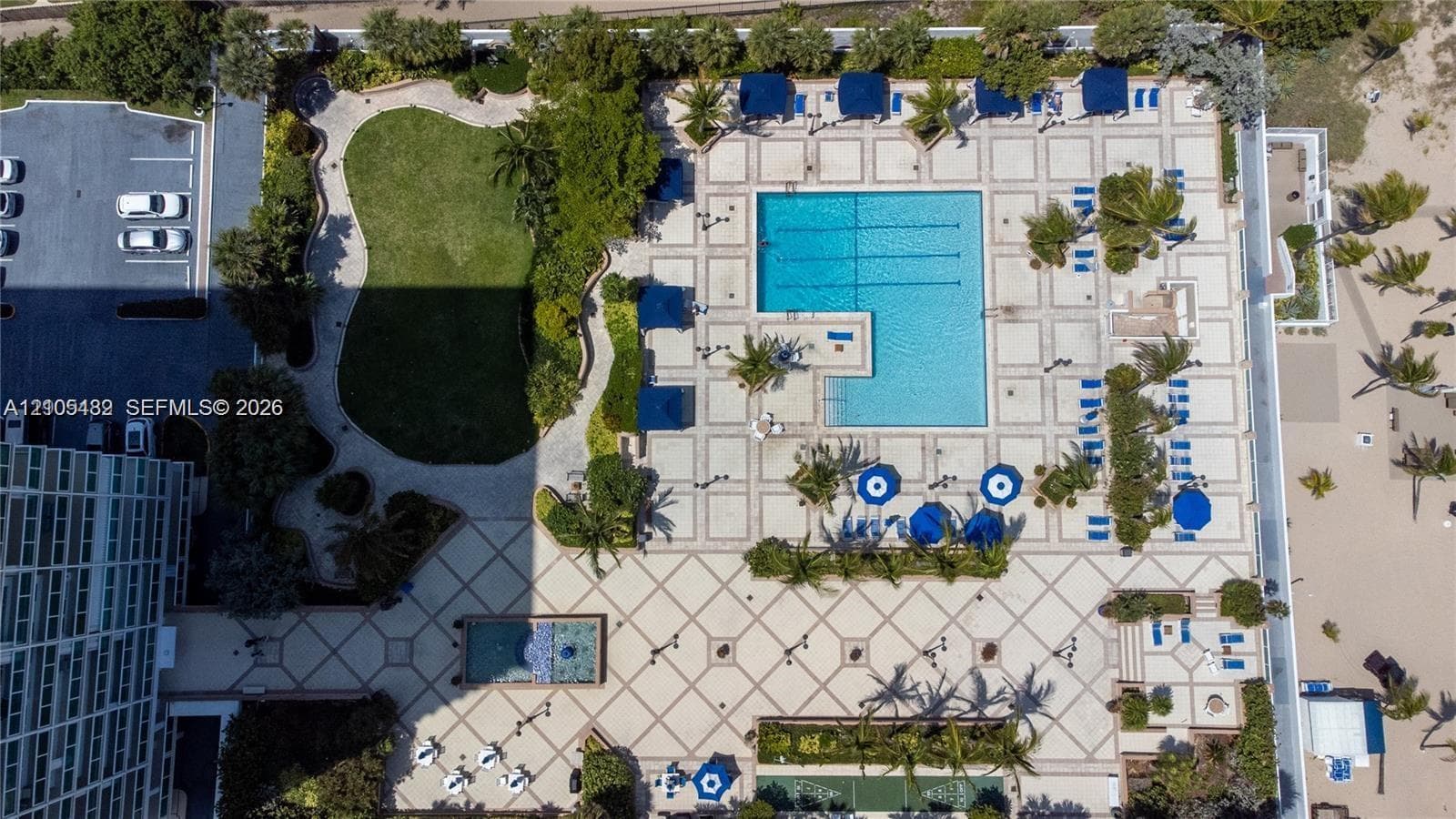 Aerial perspective of the common grounds featuring a lap pool with tiled decking, a rectangular reflecting pool, landscaped green space, and palm tree clusters