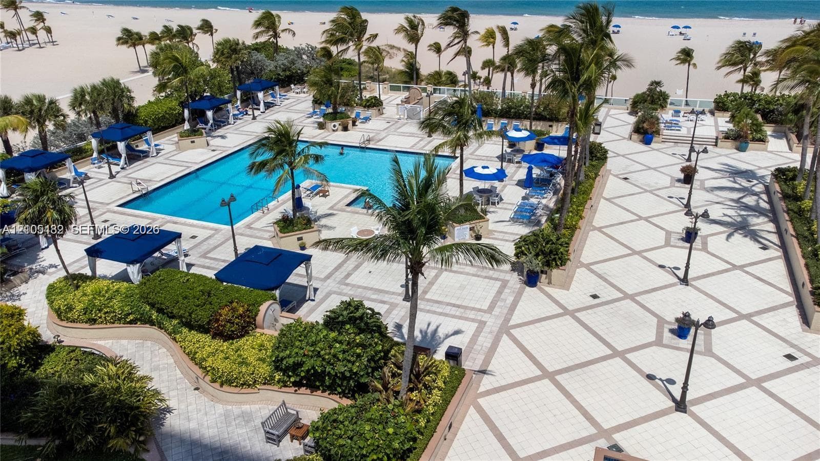 Outdoor swimming pool featuring a paved pool deck, surrounding tropical landscaping, and pole-mounted lighting