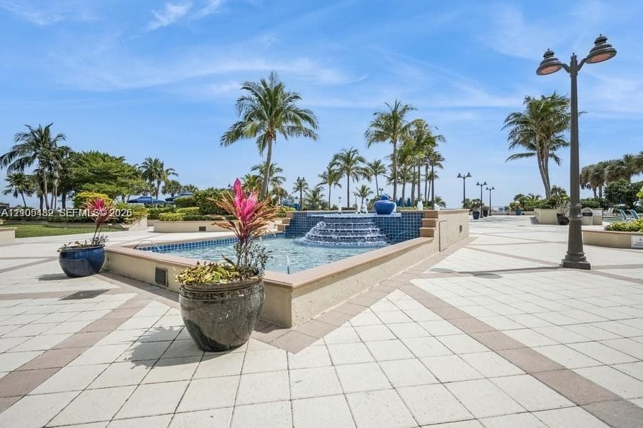 Exterior courtyard featuring a tiered fountain with blue decorative tile, paved walkways, and mature palm trees