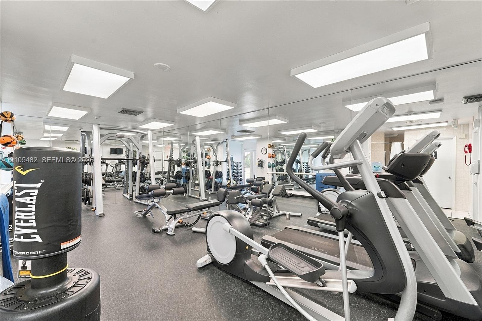 Dedicated fitness area featuring rubberized flooring, wall-to-wall mirrors, and flush-mount panel lighting