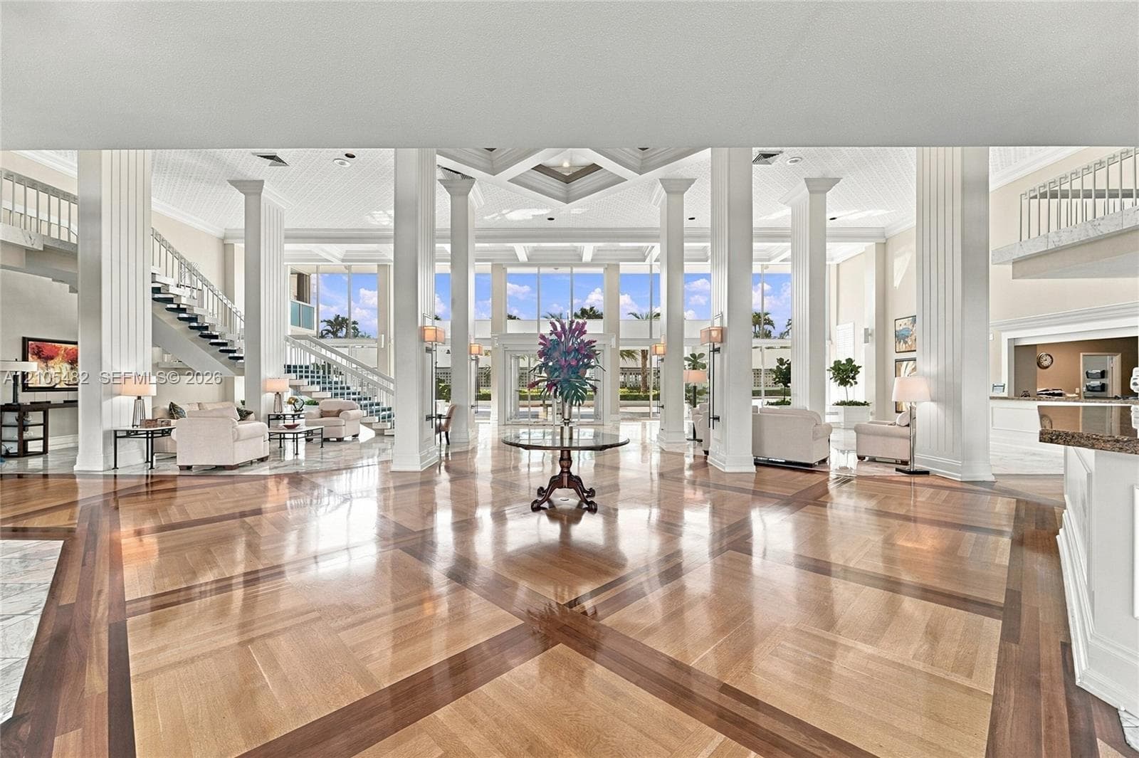 Grand foyer featuring inlaid wood-finish flooring, soaring coffered ceilings, architectural support columns, and expansive floor-to-ceiling glass windows