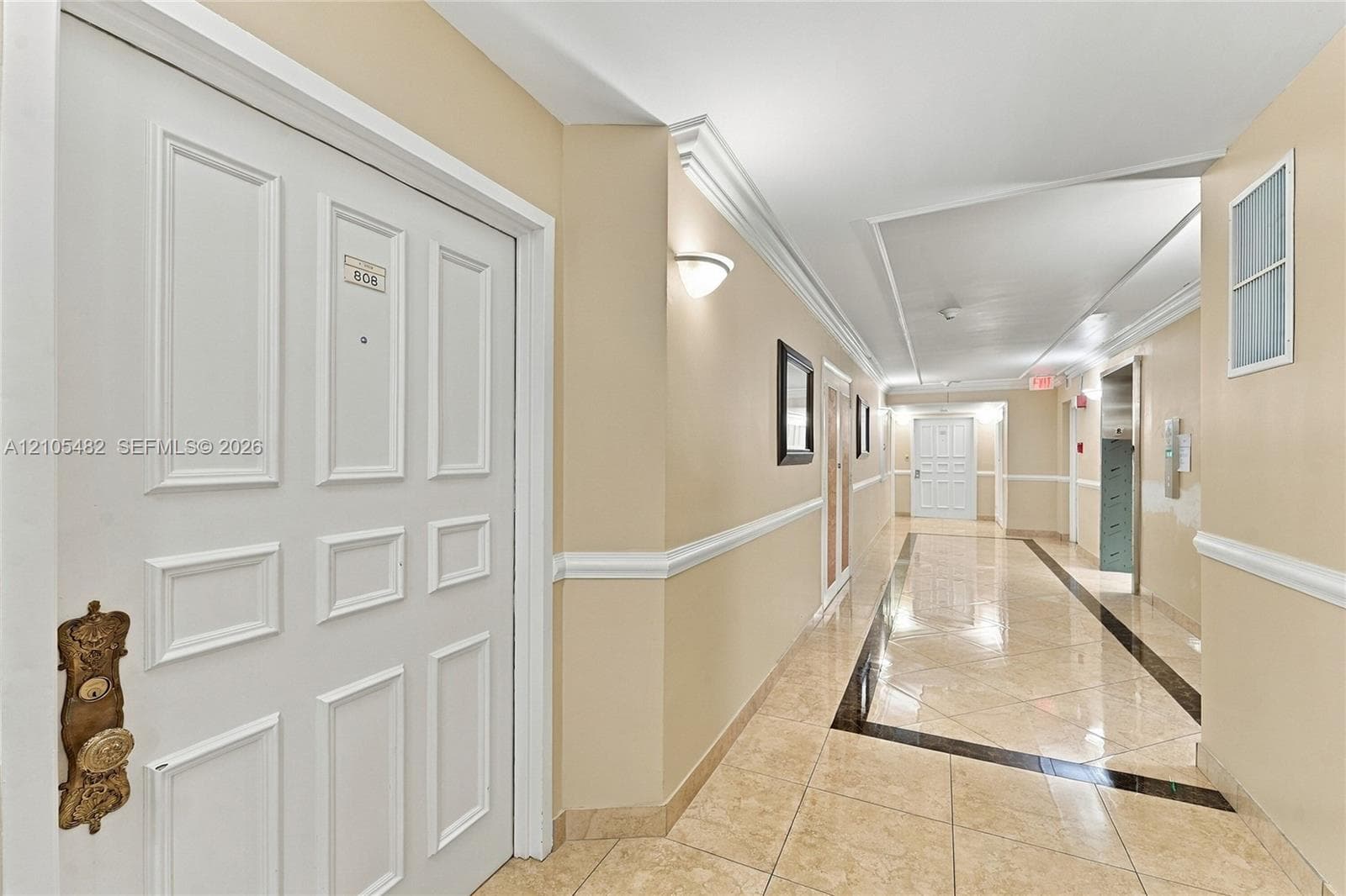 Interior hallway featuring tile flooring with decorative dark inlay, wainscoting, crown molding, and wall-mounted sconce lighting