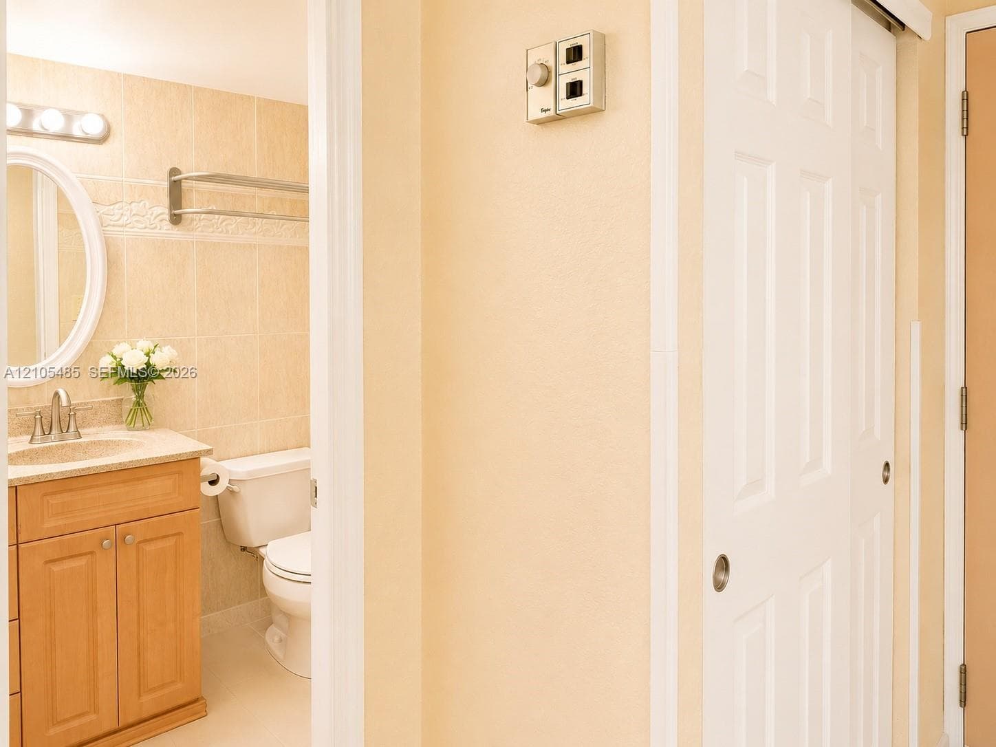 Bathroom with a wood-finish vanity, light-toned countertop, oval mirror, and tile-surround wall