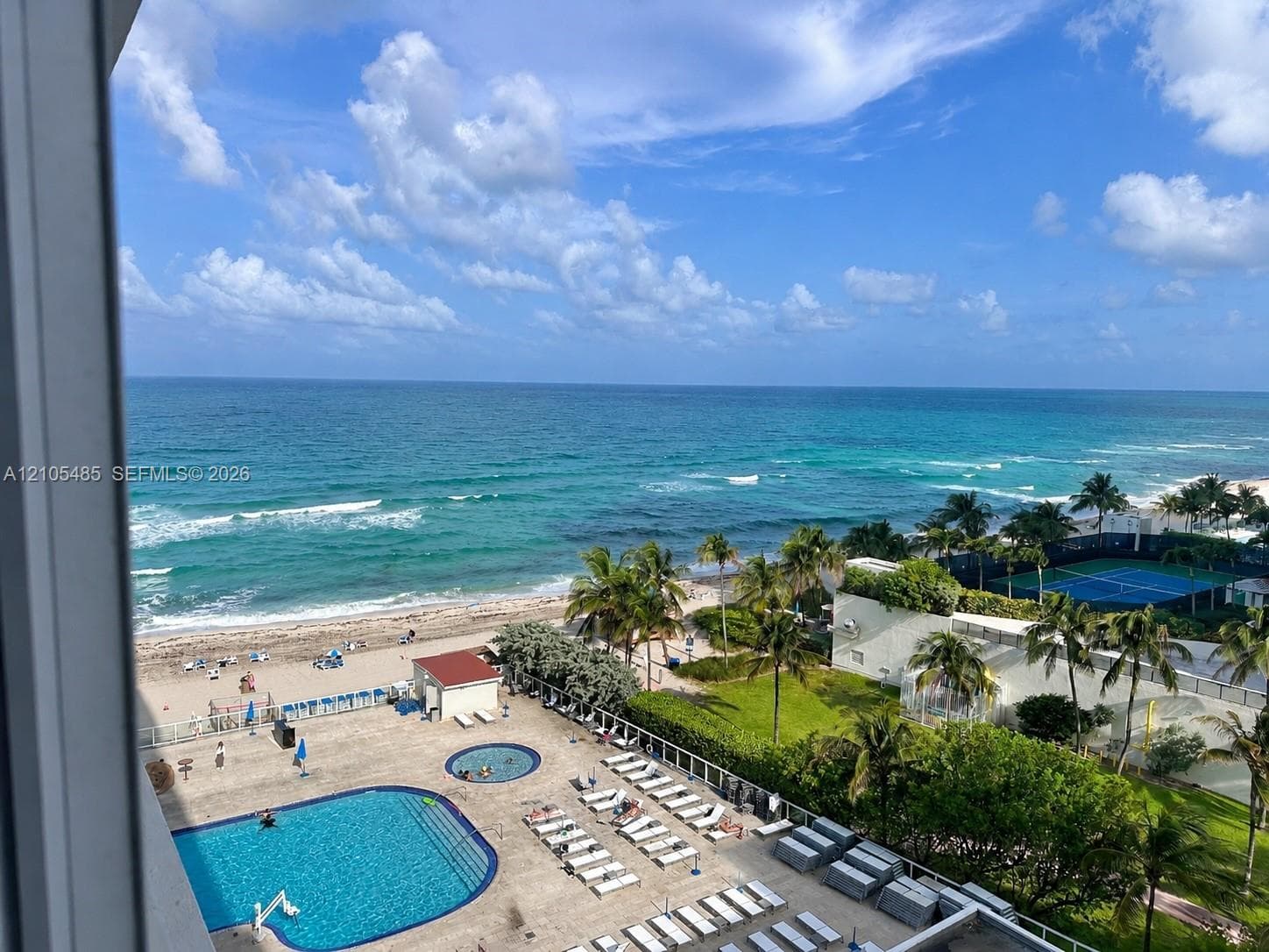 Expansive oceanfront setting featuring a sandy beach, outdoor swimming pool, tennis court, and mature palm trees
