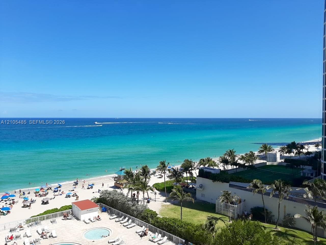 Expansive oceanfront setting featuring a sandy beach, clear blue water, and palm trees
