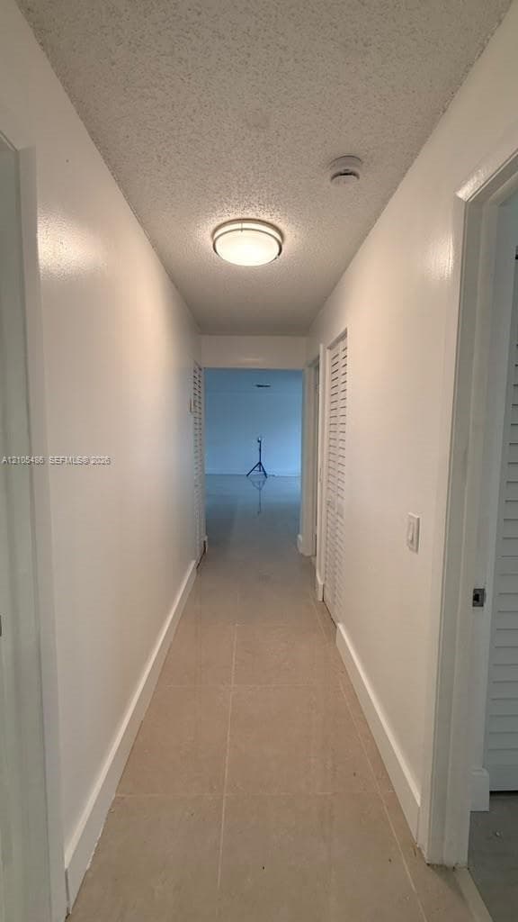 Hallway featuring neutral tile flooring, louvered bi-fold closet doors, and a flush-mount circular ceiling light