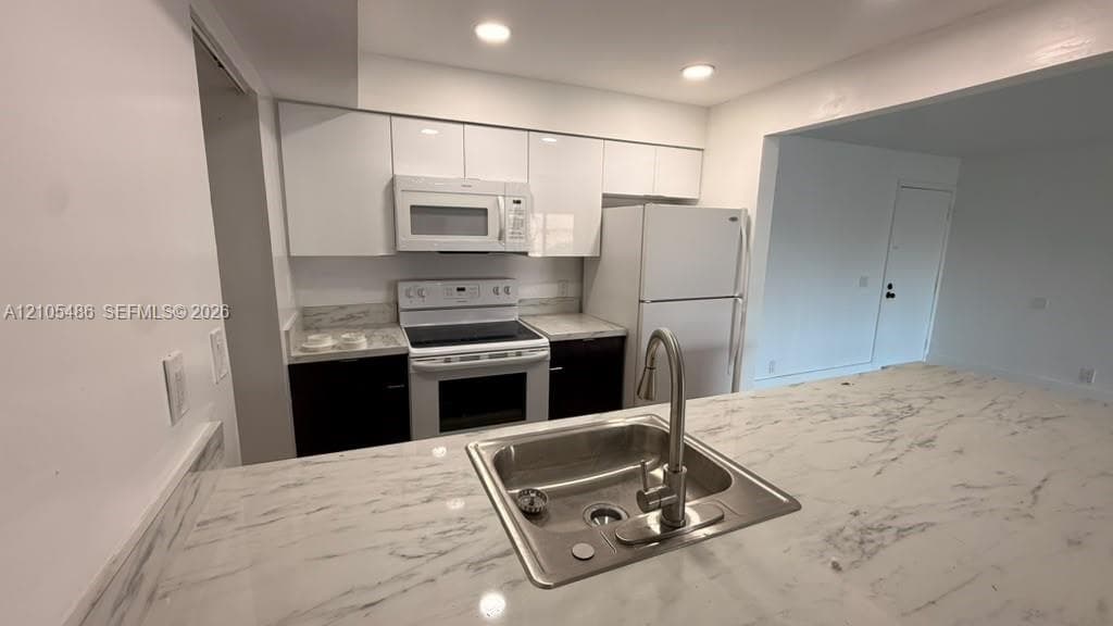Kitchen featuring high-gloss cabinetry, stone-patterned countertops, stainless steel undermount sink with a pull-down faucet, and recessed lighting