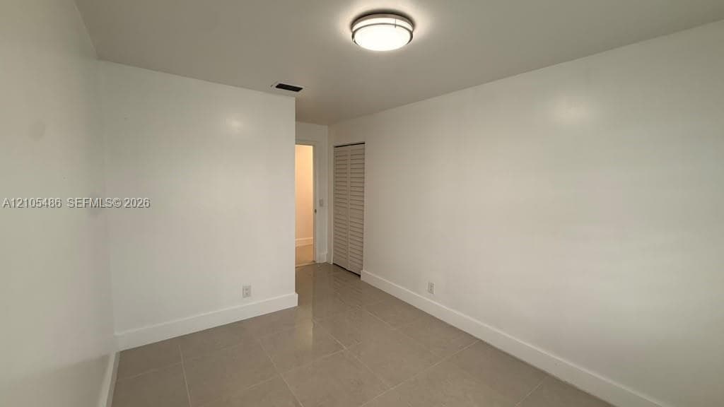 Neutral interior space featuring polished tile flooring, crisp white walls, a flush-mount circular ceiling light, and a bi-fold louvered closet door